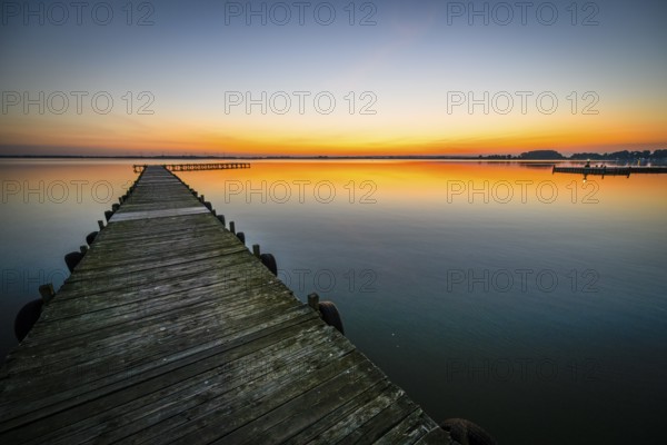 Wooden walkway leads into quiet Dümmer Lake at bright sunset, Lembruch, Dümmer See, Lower Saxony, Germany