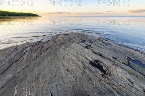 Far-reaching view of the quiet lake Vänern with gently sloping granite rocks archipelago under calm sky in the evening sunset in a peaceful atmosphere, Värmlands län, Sweden