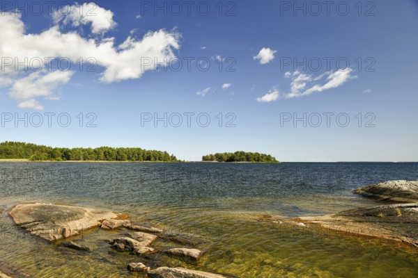 A lake with rocks in the foreground, islands on the horizon and a sky with few clouds at Lake Vänern, Värmlandsnäs peninsula, Värmlands län, Sweden
