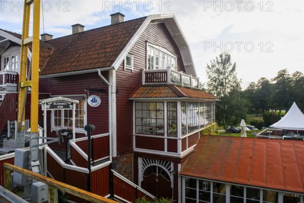 Two-storey red house with glass veranda against wooded background under blue, Sjötorp, Västra Götalands län, Sweden