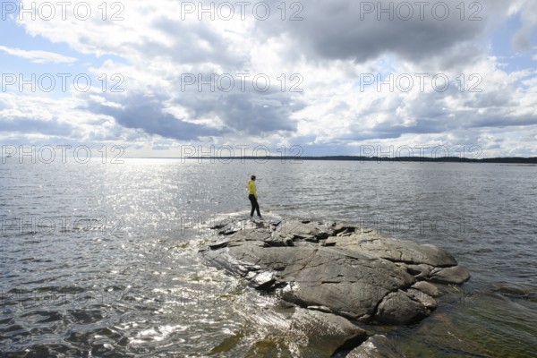 Young woman girl standing on archipelago on rocks at Lake Vänern under cloudy sky, Värmlands län, Sweden