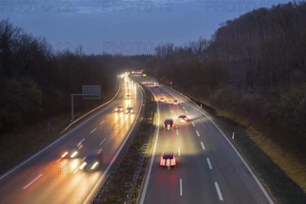 Illuminated motorway in the dark with passing cars, surrounded by hills and trees, near Stuttgart, Baden-Württemberg, Germany