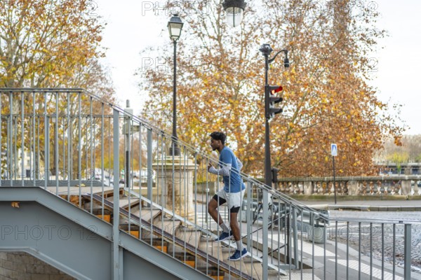 Man actively training by running up a metal staircase in a parisian urban setting, performing fitness exercise outdoors with autumn trees in the background