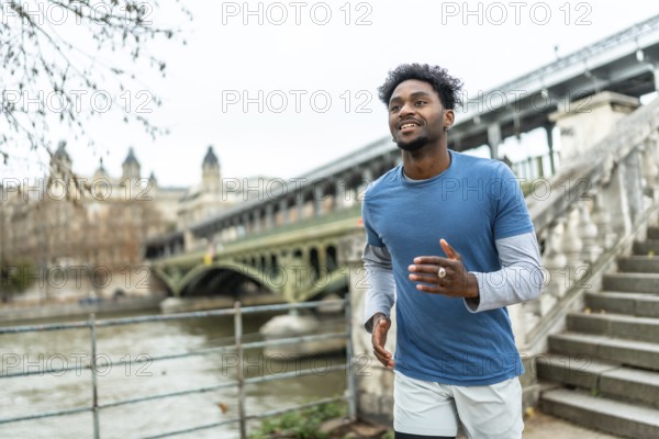 Young black man jogging along the seine in paris, training by the pont de bir hakeim with city architecture in the background, enjoying an energetic outdoor workout