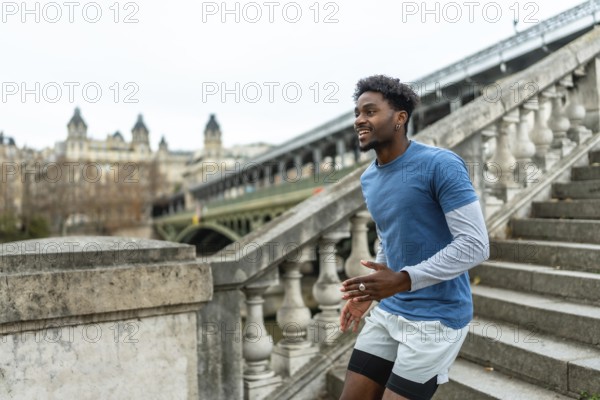 Young black man training and exercising stairs in paris, enjoying fitness and urban lifestyle with a historic bridge and city buildings in the background