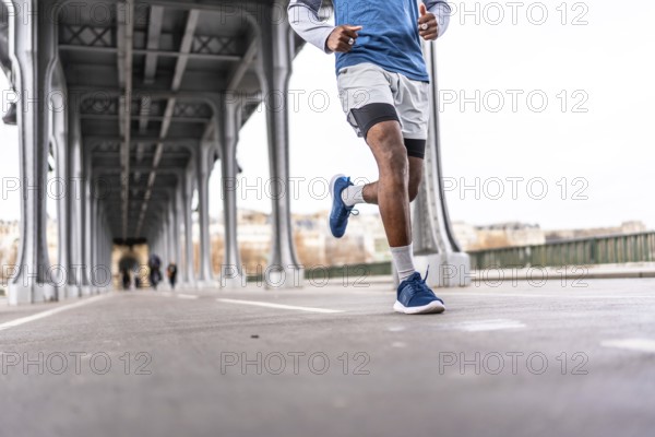 Young man running across a parisian bridge for fitness, showcasing urban training, athletic endurance and active lifestyle amid city architecture and riverbank scenery