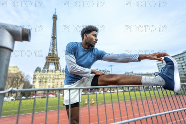 Young athletic man performing stretching exercises on a running track with the iconic eiffel tower in the background, promoting fitness and an active urban lifestyle