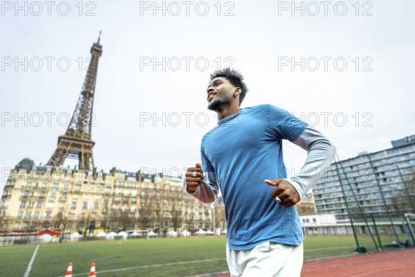 Young athletic black man training on a running track with the iconic eiffel tower and parisian buildings in the background, representing sport and wellness in urban france
