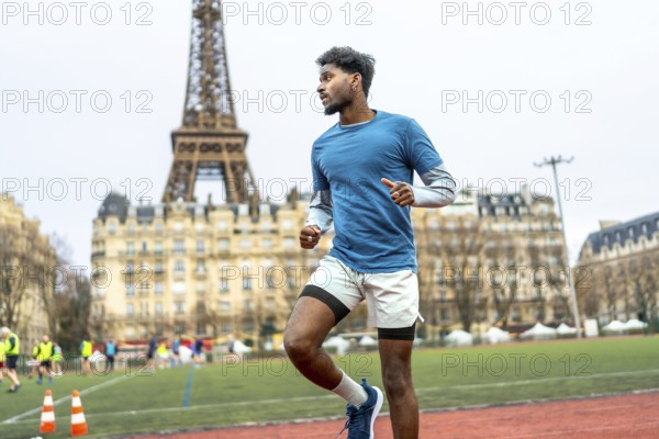 Young black man sprinting and training on an outdoor stadium track with the eiffel tower and parisian buildings in the background, focused and fit during daytime workout