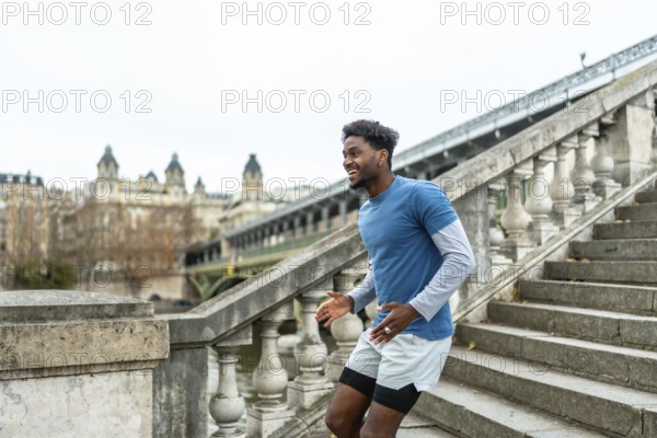 Young black man in sportswear training, laughing, and running up concrete stairs on the bir hakeim bridge, showing urban fitness and city wellness in paris