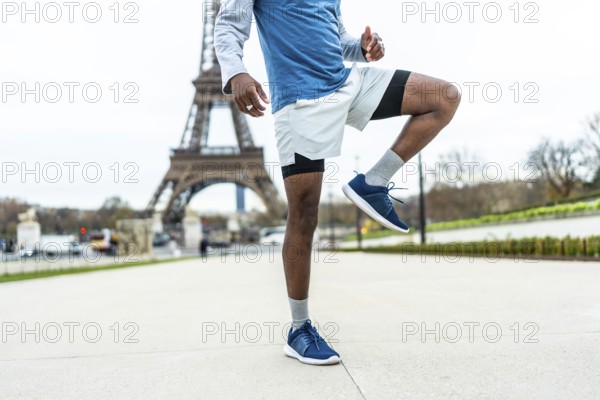 African american male athlete engaging in a high knee exercise or warm up routine, demonstrating fitness and training against the iconic backdrop of the eiffel tower in paris