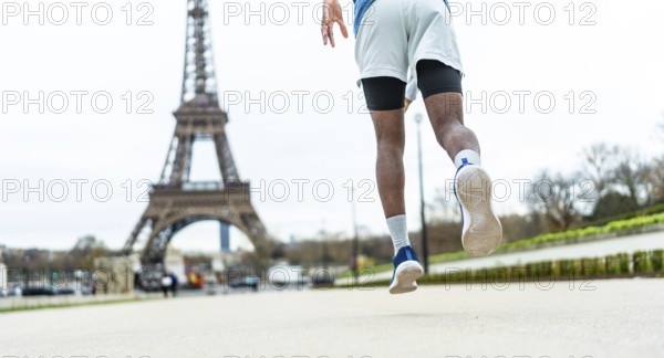 Man running on city street, elevating through a jump or stride, showcasing athleticism and an active urban lifestyle with the iconic parisian landmark in the blurred background