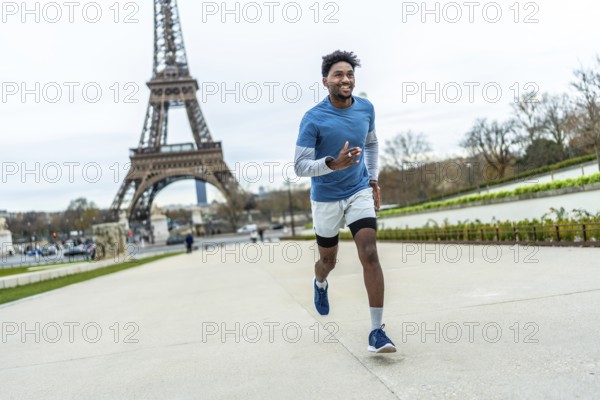 Athletic man jogging past the eiffel tower in paris, smiling and staying fit outdoors on a cloudy day, urban workout showing energy, movement and healthy lifestyle