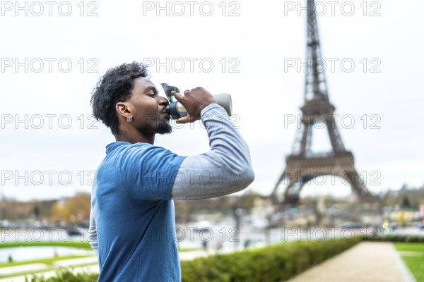Black man staying hydrated. Drinking water from a reusable bottle after a workout with the iconic eiffel tower blurring in the background. Embodying fitness and a healthy lifestyle in an urban setting