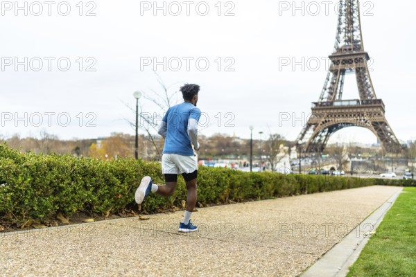 Man actively running along a path in paris, maintaining his fitness and enjoying urban sports with the iconic eiffel tower prominently featured in the background under a cloudy sky