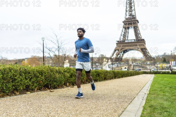 Young man actively jogging along a pathway in a parisian park, focusing on health and fitness with the iconic eiffel tower in the background, representing exercise in a global city
