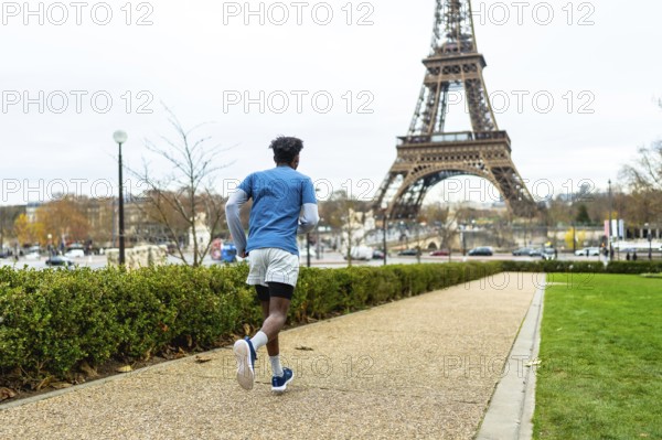 Young man exercising outdoors on a gravel path in paris, enjoying a fitness run with the iconic eiffel tower in the background, promoting active urban lifestyle and tourism