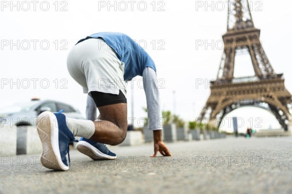 Athlete in starting position, poised for a run on an urban street, training for speed and performance in the iconic cityscape of paris with the eiffel tower in the background