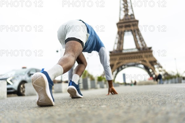Male athlete in starting block position preparing for a sprint on a city street, with the iconic eiffel tower in the background, symbolizing urban fitness and ambition