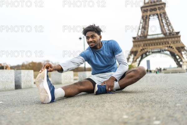 Young black man stretching on the ground, preparing for exercise with the iconic eiffel tower in the background, promoting fitness and an active lifestyle in an urban environment