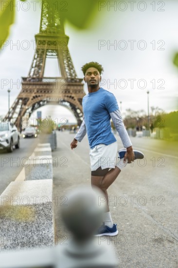 Young black man in sportswear stretching before a workout, standing on a sidewalk with the eiffel tower in the background, embodying health and well being in an urban environment