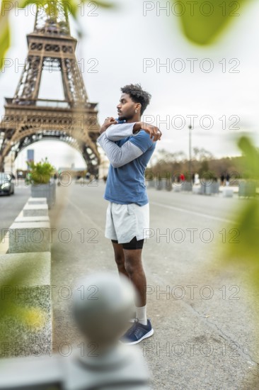 Young athletic man stretching his arms and shoulders on a city street in paris, preparing for an urban run with the iconic eiffel tower visible in the background