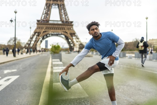 Young athletic man stretching his leg on a low wall, preparing for a workout session with the iconic eiffel tower prominently featured in the background, embodying fitness and urban exploration