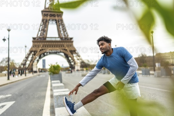 Fit young black man performing leg stretches in an urban environment with the eiffel tower in the background, focusing on fitness and wellbeing in the city