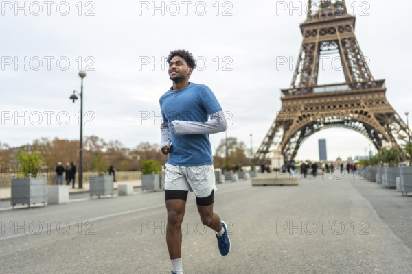 Young adult man with an arm prosthesis is running and smiling along the seine river with the iconic eiffel tower in the background, enjoying his fitness activity outdoors