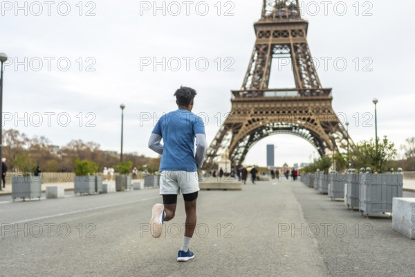 Young man running for fitness and healthy lifestyle in an urban park, exercising with the iconic eiffel tower in the background, promoting active tourism and wellness in the city