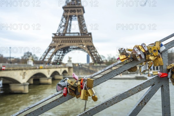 Many padlocks symbolizing everlasting love are attached to a bridge railing, with the iconic eiffel tower and seine river creating a romantic background in paris, france