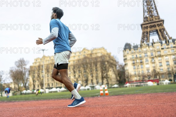 Black man engaging in physical activity, jogging for fitness and health on a tartan track in an urban environment with european buildings and the iconic eiffel tower in the background