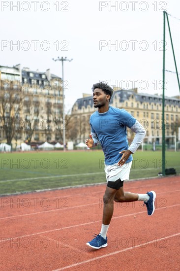 Male athlete with dark skin running on an urban athletic track, training for endurance and maintaining fitness with european buildings in the background