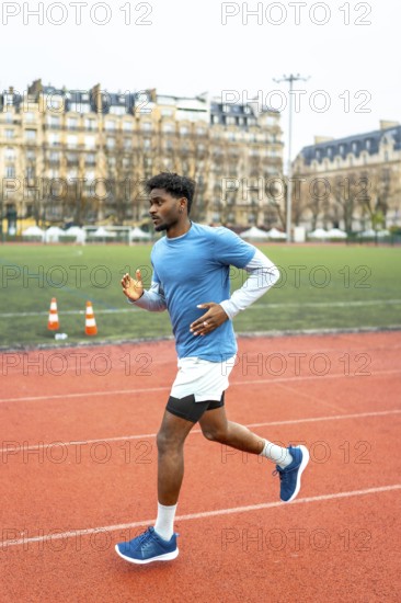 Young dark skinned athlete sprinting on a red urban track in paris, full body side view capturing motion, endurance and fitness in daytime city sports field with architecture backdrop