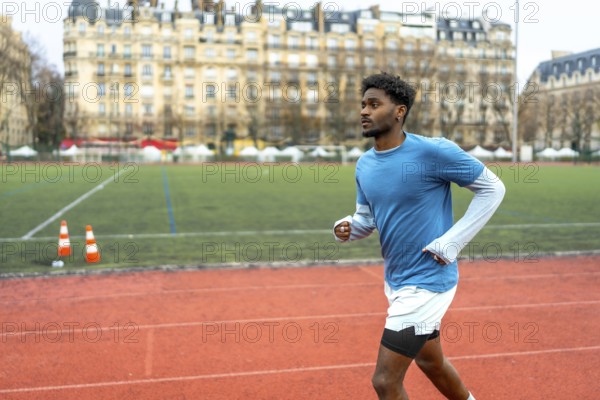 Young black man training on a running track with historic parisian buildings in the background, representing sport, fitness, and an active lifestyle in an urban environment