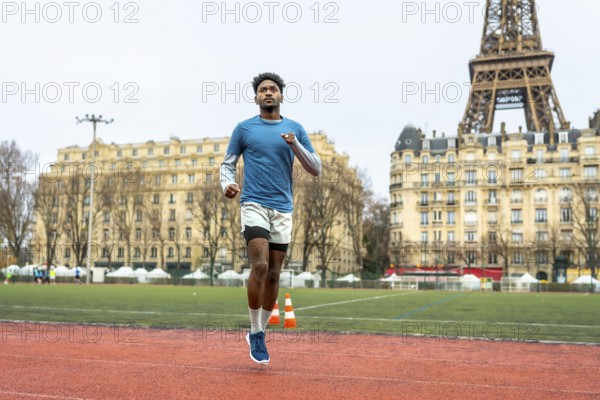 Young athletic man running on an outdoor track in paris, focusing on urban sport performance and fitness training with a famous landmark in the background