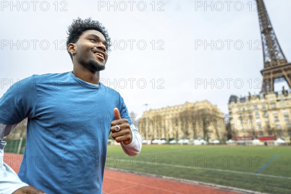 Young black man smiling and jogging outdoors on a running track with the iconic eiffel tower and parisian buildings in the blurred background, embodying urban fitness and healthy lifestyle