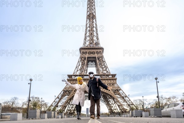 Happy young couple posing joyfully in front of the eiffel tower in paris, experiencing a romantic and memorable european city break together, dressed in warm winter clothing