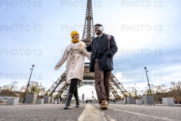 Diverse couple walking outdoors in paris holding hands, enjoying a romantic trip together on a winter day with the iconic eiffel tower in the background