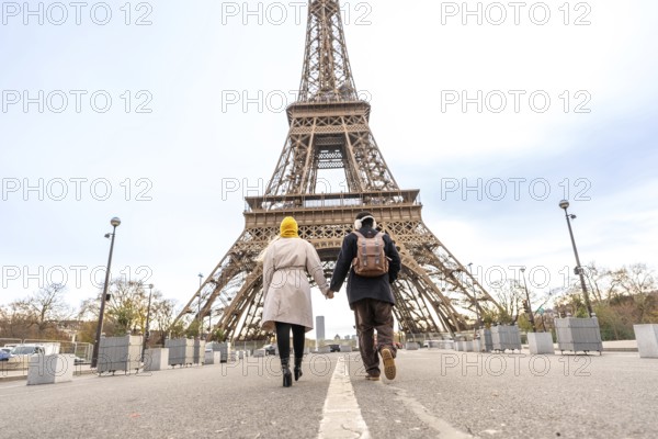 Adult male and female travelers holding hands and walking together towards the iconic landmark in paris, symbolizing romance, travel, and shared adventure