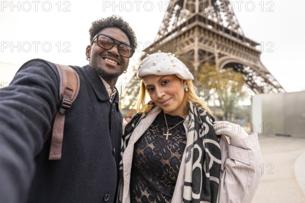 Diverse couple smiling for a close up selfie in front of the eiffel tower, embracing travel and romance on a stylish paris city break, enjoying winter coats and scarves