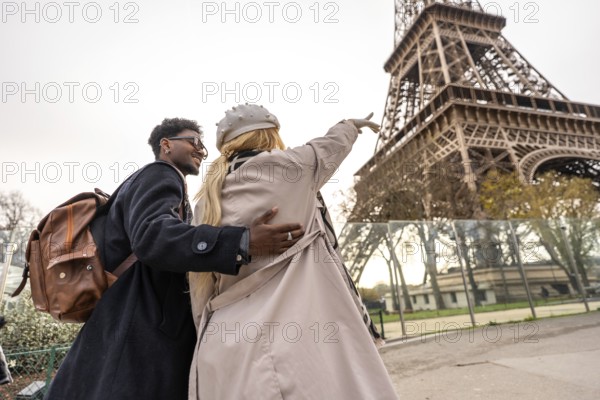 Young diverse couple traveling together, smiling and pointing out a landmark while visiting the scenic city of paris, embracing discovery and romantic travel