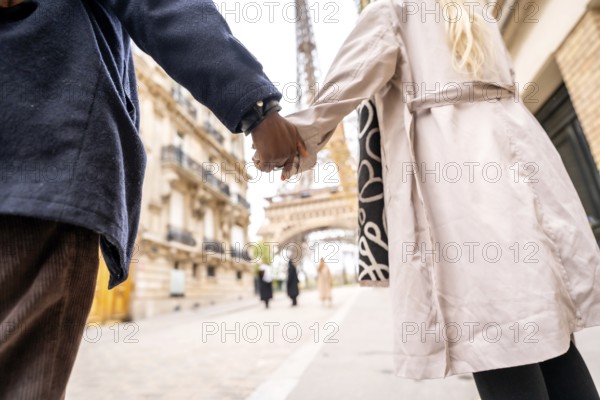 Couple holding hands walking toward the eiffel tower in paris, capturing romance, travel and togetherness on a city street with blurred landmark in the background