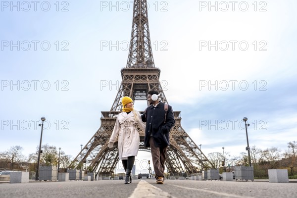 Young diverse couple walking and smiling together in front of the eiffel tower, embracing romance, tourism, and travel in the iconic city of paris, france