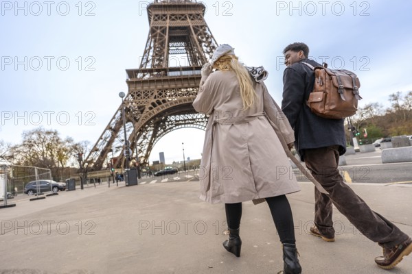 Young diverse couple exploring a european city landmark, pulling luggage and wearing stylish trench coats, enjoying a romantic tourism trip and urban adventure