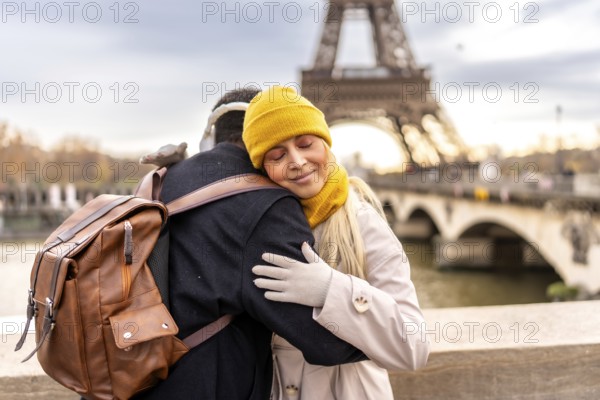 Young diverse couple embraces on a paris bridge, sharing a tender moment with the eiffel tower and seine softly blurred in the winter cityscape background
