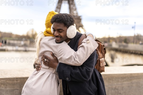 Diverse couple embracing outdoors in paris, smiling with joy and affection as they celebrate travel and romance near the seine and eiffel tower during a winter city getaway