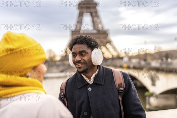 Young diverse couple interacting and smiling during their winter vacation in paris, travelers exploring the city with the iconic eiffel tower in the background