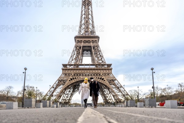 Couple walking hand in hand toward the eiffel tower in paris on a cloudy day, sharing a romantic moment while exploring the city's iconic architecture and sightseeing charms