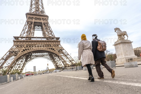 Young couple walking on a street, seen from behind, enjoying a romantic trip to the eiffel tower, iconic french landmark and a symbol of love and tourism